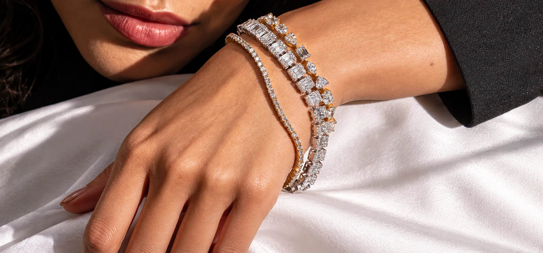 Close-up of a wrist wearing layered bracelets, resting on white satin in sunlight