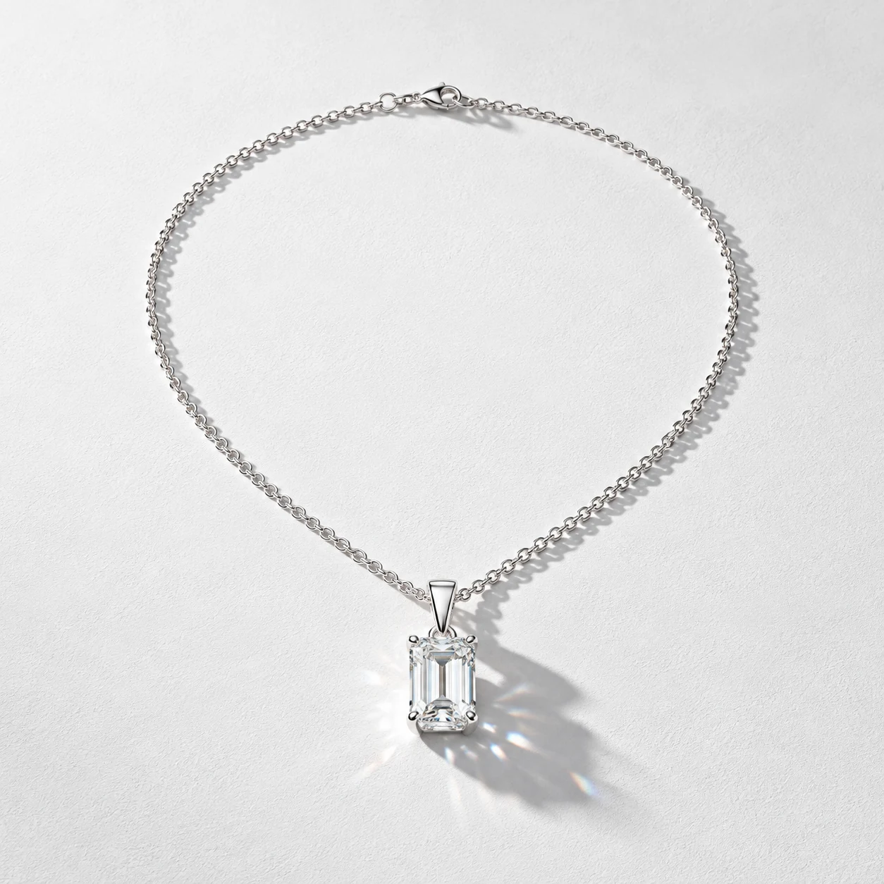 A rectangular-stone pendant and chain arranged on a white textured background